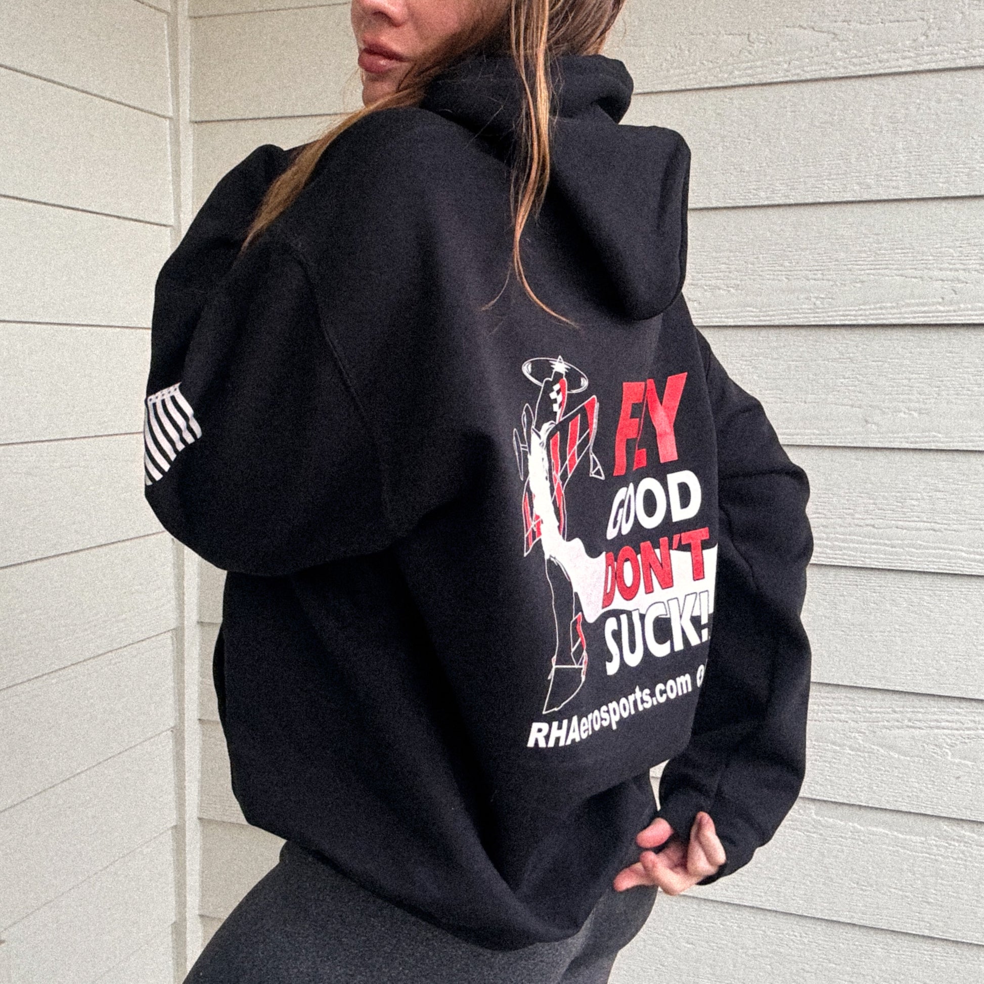 woman wearing an oversized hooded black sweatshirt  with Rob Holland Aerosports logo visible on the back and the phrase "Fly Good Don't Suck" and www.rhaerosports.com website 