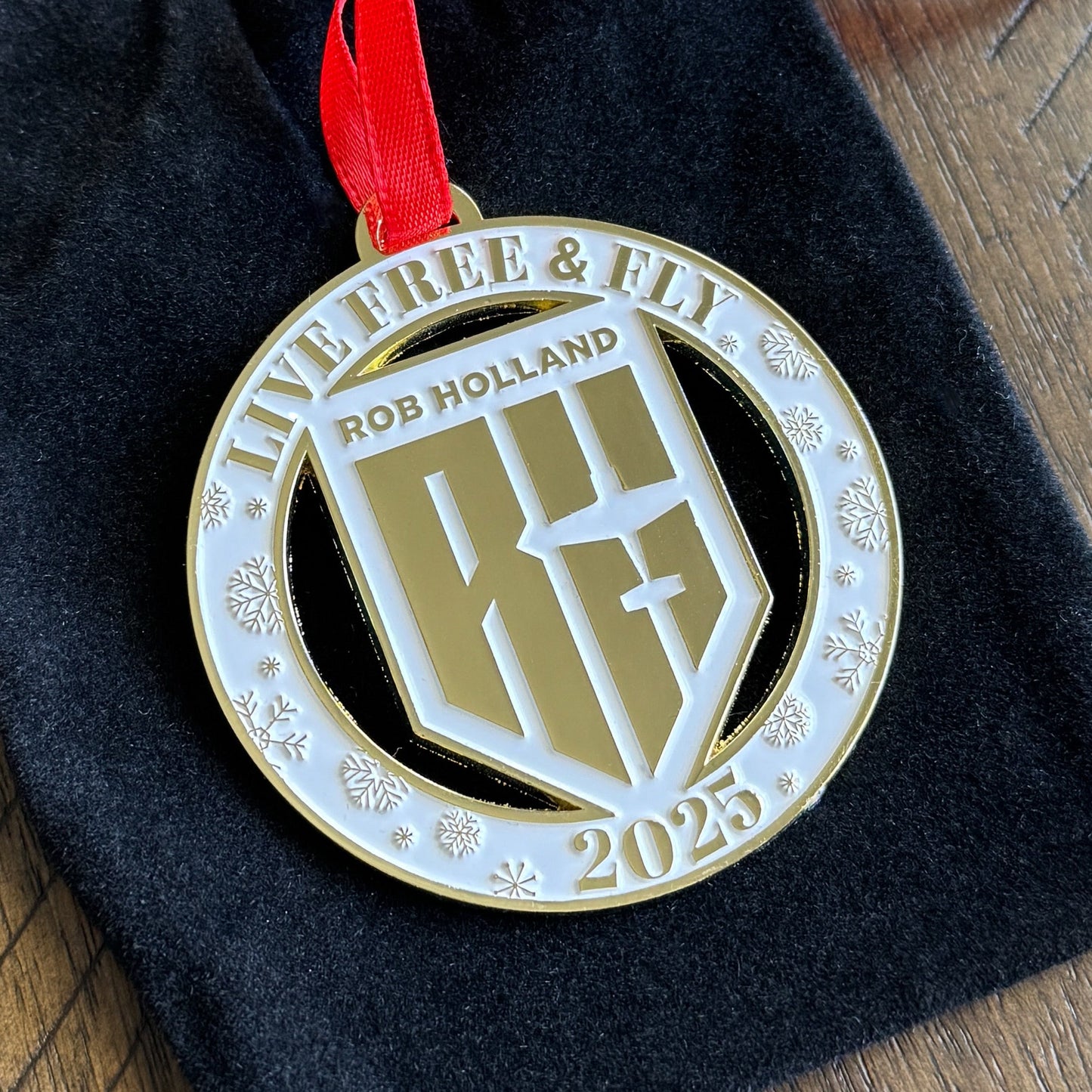 Gold and white medal with 'Rob Holland' logo and '2025' on a red ribbon, placed on black fabric.